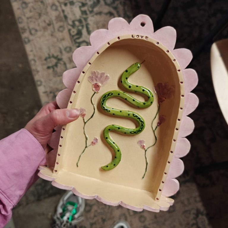 Handhoudend een decoratief altaartje met een groene slang en bloemenmotieven.