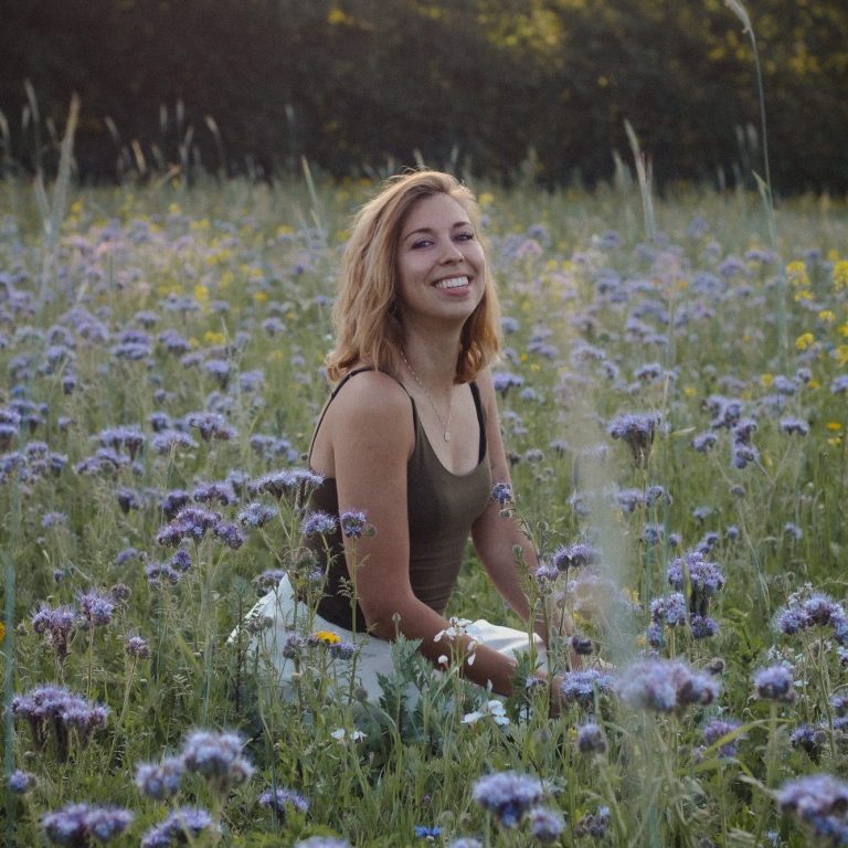 Vrouw in een groene jurk met bloemenprint, staand in een weelderige, groene omgeving.
