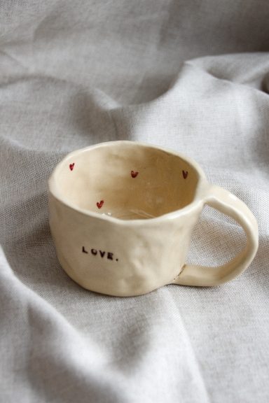 A hand-crafted beige mok met rode stippen en het woord 'love' erop.