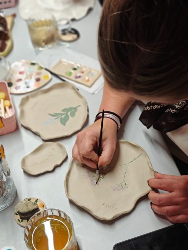 Een persoon schildert op een onbewerkt aardewerk oppervlak met een penseel.