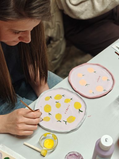 Een vrouw schildert gele citroenen op een bord van keramiek