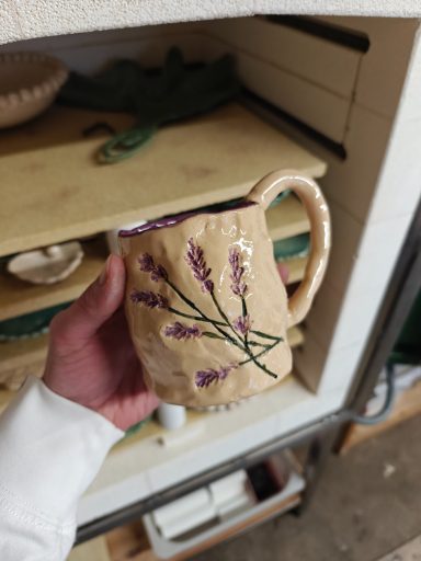 Aardewerk mok met paarse lavendelmotieven, vastgehouden door een hand.