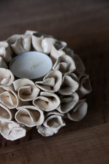 Theelicht houder met decoratieve bloemenring van beige materiaal.