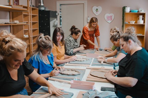 Groep vrouwen werkt samen aan klei-projecten in een creatieve workshop.