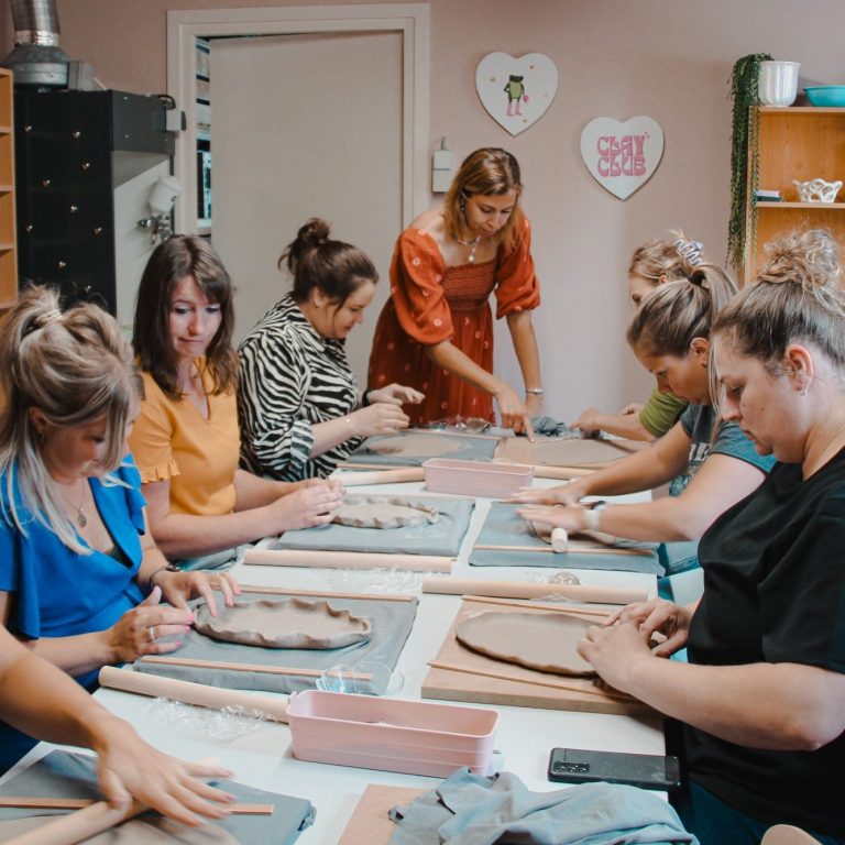 Vrouwen maken keramiek tijdens een creatieve workshop aan een lange tafel.