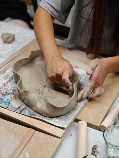 Een persoon vormt een schaal van klei met beide handen op een werkblad.