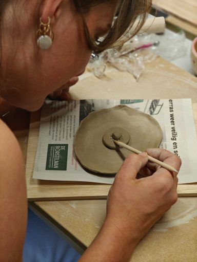 Een persoon maakt een keramisch object met een penseel op een werkblad.