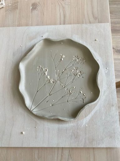 A beige, scalloped clay plate with delicate pressed flowers embedded.