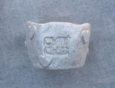 Witte klei object met een gegraveerd symbool en ronde hoeken.