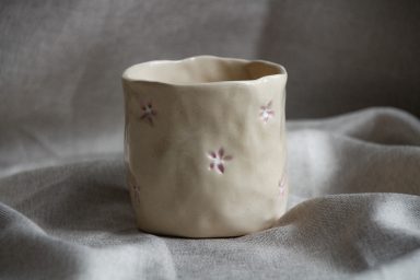 Handgemaakte, onregelmatige keramische beker met kleine bloemen.