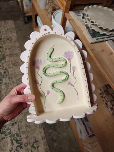 Handgemaakt keramisch bord met een groene slang en bloemenmotief.