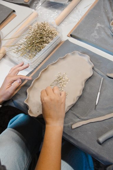 Een hand die decoratieve takken op een kleiplateau plaatst tijdens een creatieve sessie.