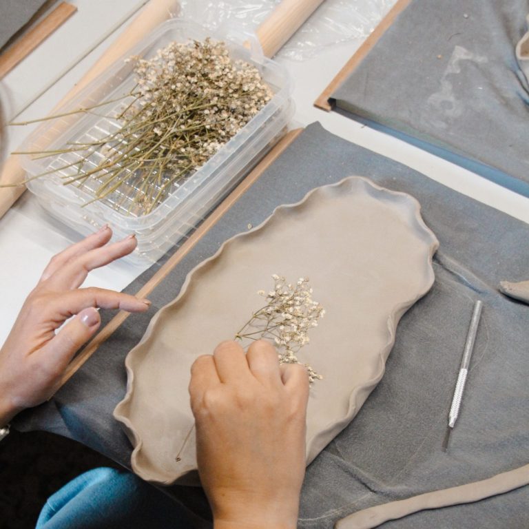 Handen bewerken klei met een takje bloemen op een werkblad.