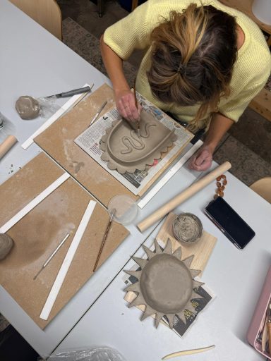 Vrouw werkt met klei op een tafel met verschillende materialen rondom.