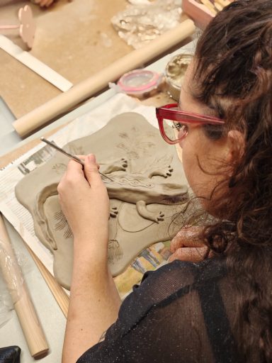 Vrouw met rode brillen maakt een kleimodel met een penseel.