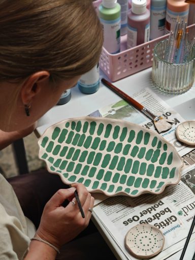 Vrouw schildert met groene verf op een keramisch bordje met een golvende rand.