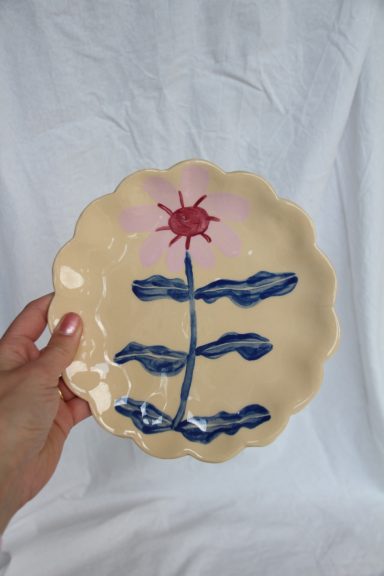 Handgeschilderd bord met een bloemmotief in roze en blauw op een beige achtergrond.