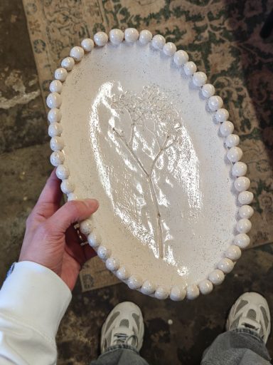 Een hand houdt een ronde schaal vast met een reliëf van een boom.