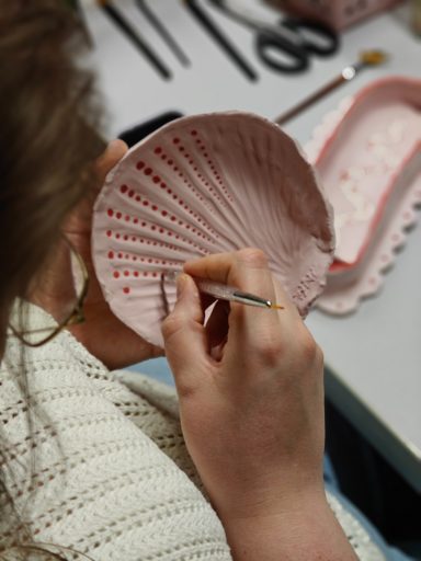Een hand verft een roze schaal met een penseel, met een focus op het detail.