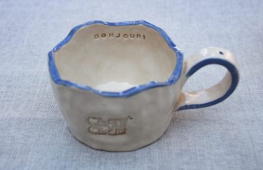 Handgemaakte keramische mok met een golvende rand en blauwe accenten.