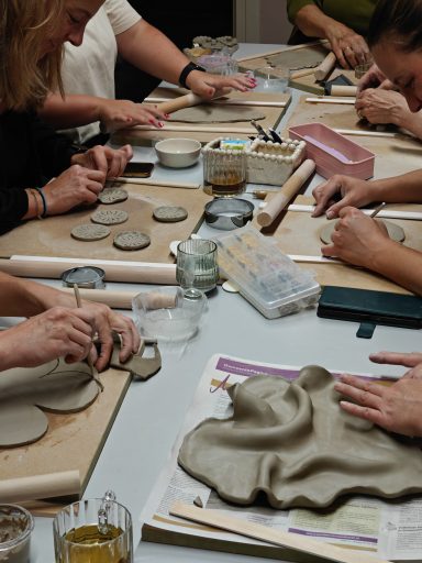 Groep mensen die klei bewerkt op een tafel, met verschillende gereedschappen en materialen.