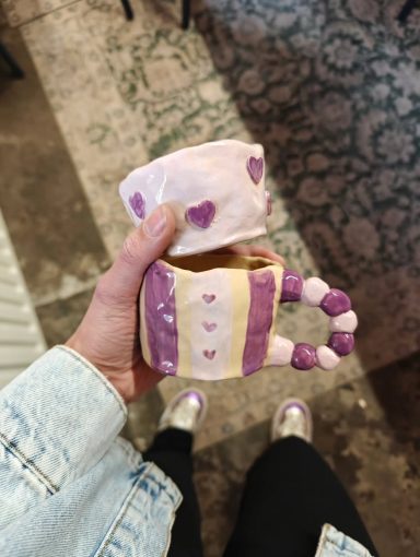 Een handgemaakte mok in paars en wit met een gestreepte handgreep.