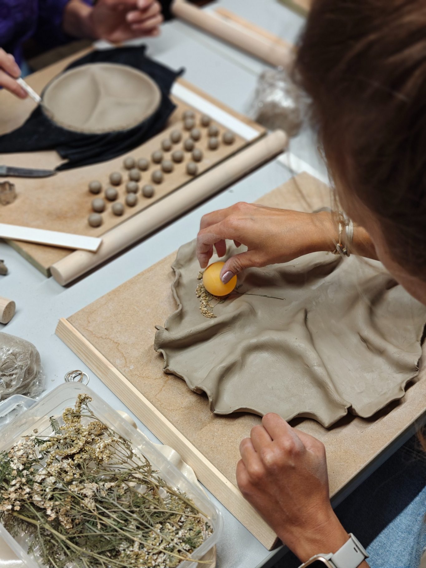 Persoon boetseert met klei en een eiervorm, omringd door andere materialen en gereedschap.
