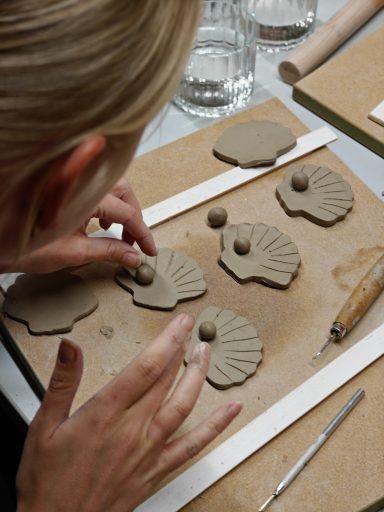 Vrouw maakt keramische schelpen van klei op een werkblad.