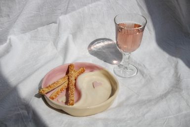 Een roze drankje in een glazen beker met een bordje koekjes op een lichte ondergrond.
