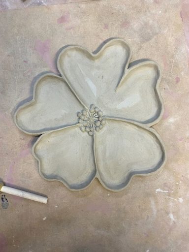 Lichtgekleurde, bloemvormige schotel met vijf bloemblaadjes en een centrale decoratie.