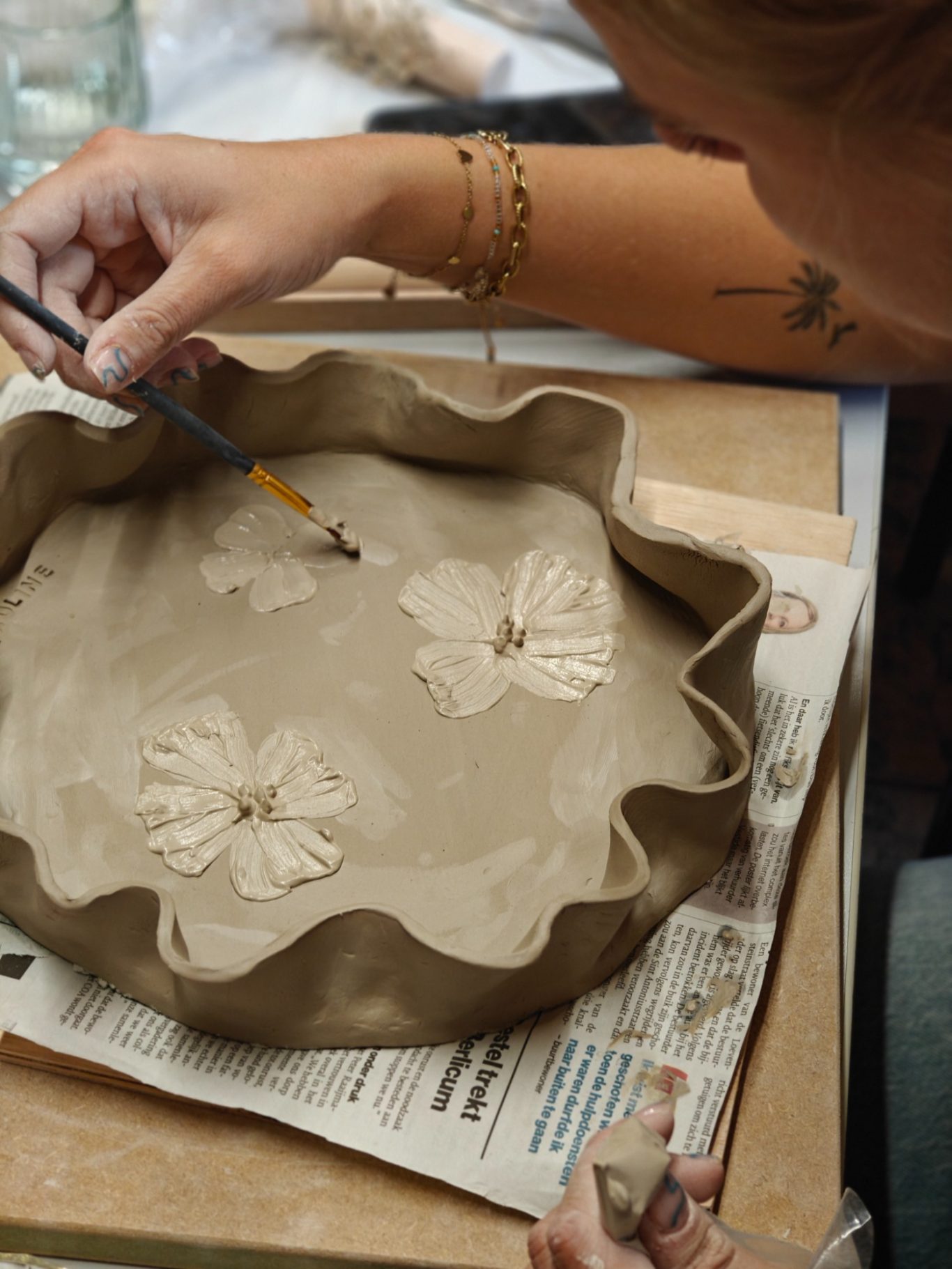 Vrouw die een rond, gegolfd kleiplaatje versiert met bloemenmotieven.