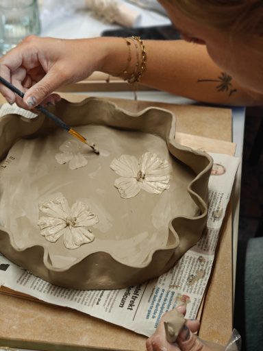 Een persoon maakt een klei schaal met bloemen.