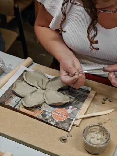 Een persoon maakt een sculptuur van klei met gereedschap op een werkblad.