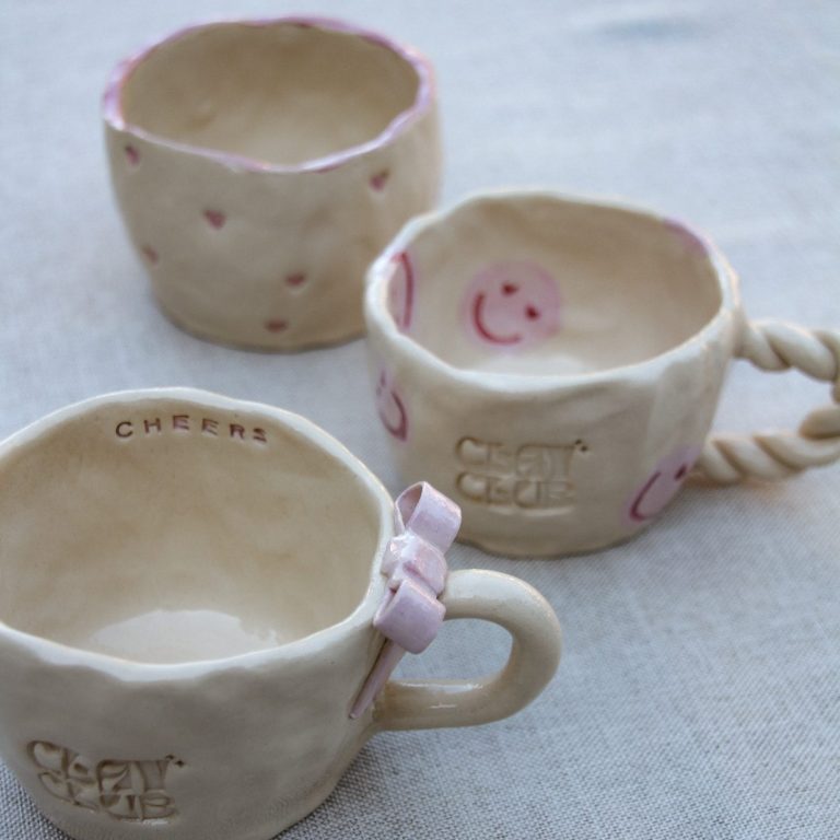 Drie handgemaakte keramische bekers met verschillende ontwerpen en kleuren.